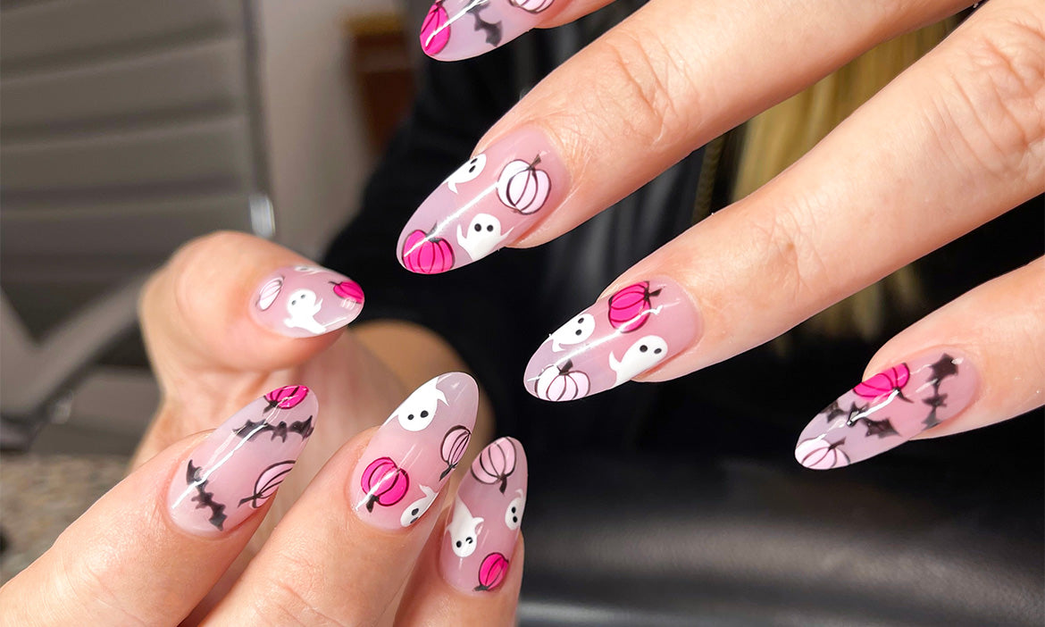 Close-up of pink Halloween-themed nail art featuring white ghosts, pink and white pumpkins, and black bats on glossy almond-shaped nails.